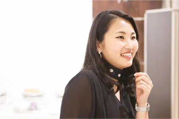 会議室で、スクリーンの前に座り、穏やかに微笑みながら話を聞いている女性