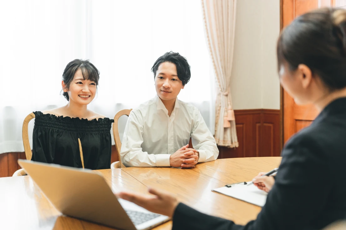 テーブルで話し合う笑顔のカップルと、クリップボードにメモを取るコンサルタント