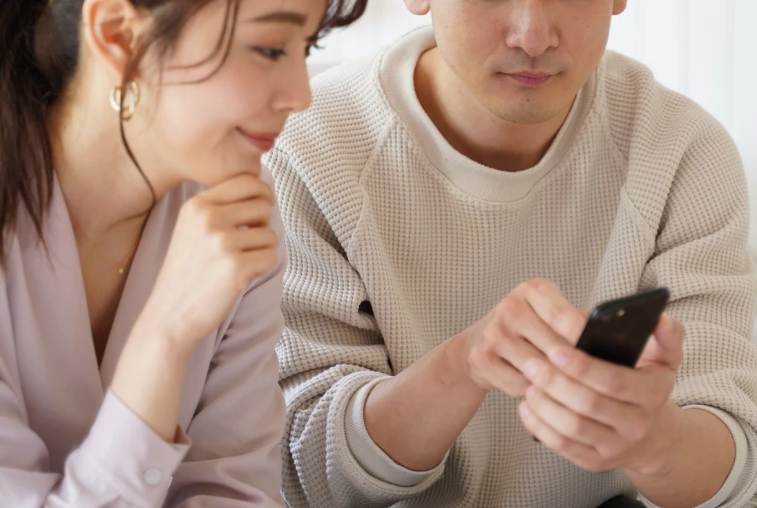 スマートフォンの画面を一緒に見ている男女。女性は微笑み、男性がスマートフォンを持って画面を見ている様子